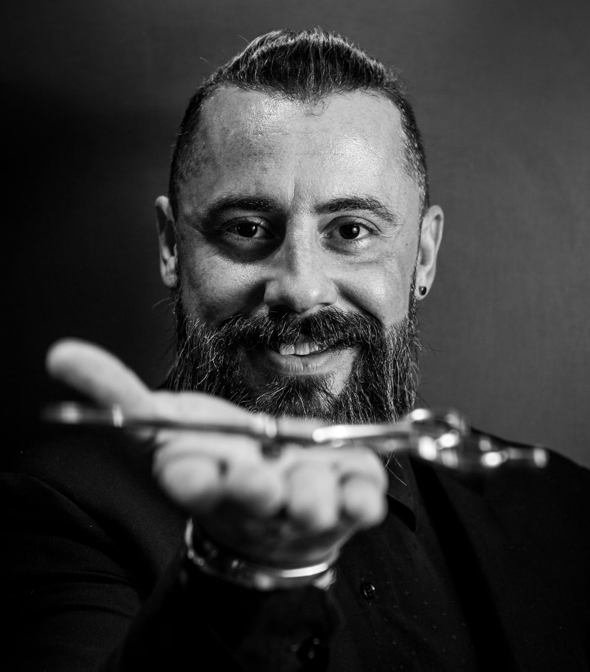 Tomás holding a pair of shears against a dark background