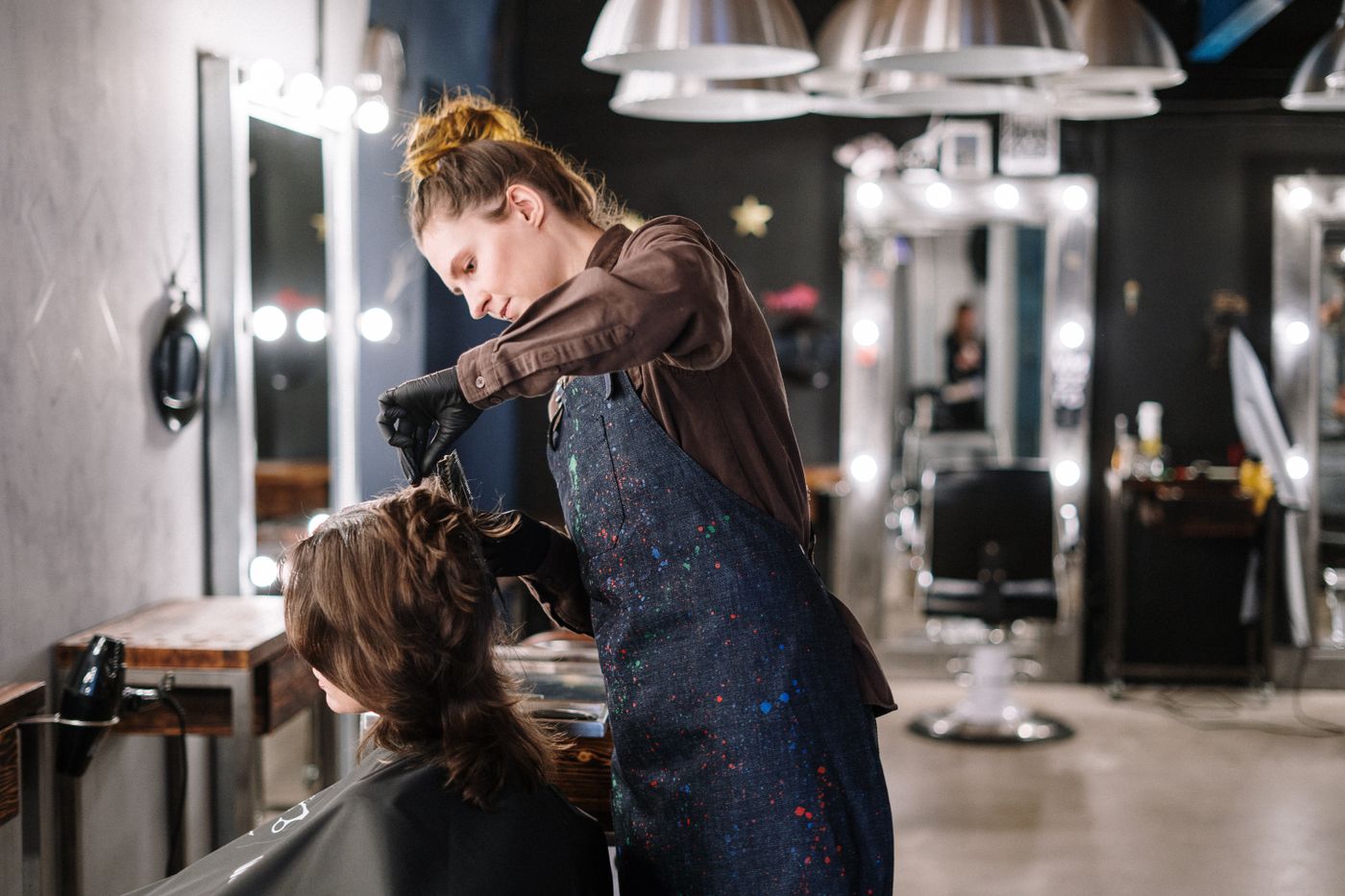 A stylist blow-drying a client's hair in a dark salon