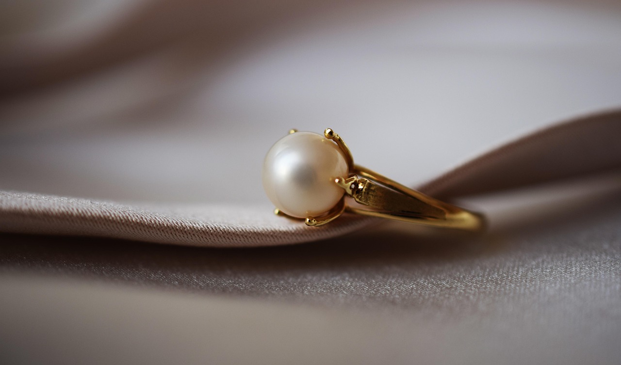A pearl ring resting on champagne silk